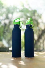 Two blue minimal reusable water bottle is sitting on a wood table with natural sunlight