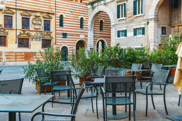 Outdoor summer cafe tables and chairs outside in old town square Piazza dei Signori, Verona city, Veneto, Italy. Italian square with sidewalk restaurant and colorful buildings