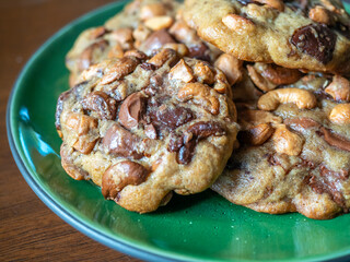 Home made big crunchy soft chocolate cookies with cashew nuts fresh baked on green plate on wooden dining table