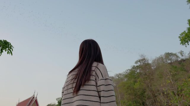Asian woman looking at flock of bats flying from cave in the evening