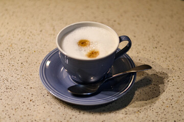 fresh cappuccino or coffee with milk in a blue cup and teaspoon