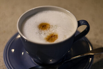 fresh cappuccino or coffee with milk in a blue cup and teaspoon