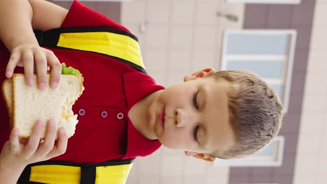 child kid boy eats sandwich with a school backpack on her back, leisure eating child, sandwich break boy, child nourishment outside, school day snack, wearing backpack child, residential background