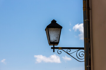 Vintage street lamp against blue sky. An old-fashioned black metal street lamp mounted on a...