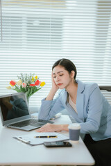 An Asian businesswoman sits at her desk, exhausted from working for a long time.