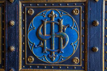 A close-up shot of an ornate door detail featuring an intertwined monogram or symbol in gold...