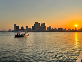 A panorama view of the city skyline while crossing the Mekong river in Phnom Penh, Cambodia - with a ferry in the river at sunset