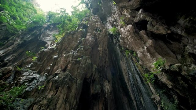 Sunlight streaming through batu caves entrance, highlighting verdant tropical foliage surrounding limestone cavern opening in malaysia