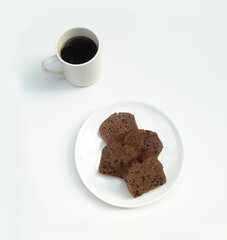 ブラックコーヒーが入った白いマグカップと白い皿の上の4切れのチョコレートブラウニー。白背景。