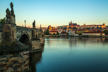 A stone bridge with statues lining its edge spans a wide river, offering a distant view of a...