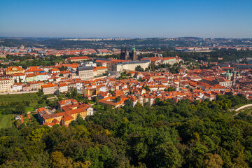 Obraz premium A panoramic cityscape view from a high vantage point, showcasing a sprawling city with red-roofed buildings, a large complex of structures, and a distant skyline under a clear blue sky.