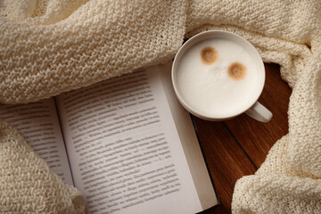 Warm cup of coffee, open book, beige soft warm blanket next to the window in autumn. Cozy sweet home atmosphere. Нygge lifestyle concept. Cozy fall mood