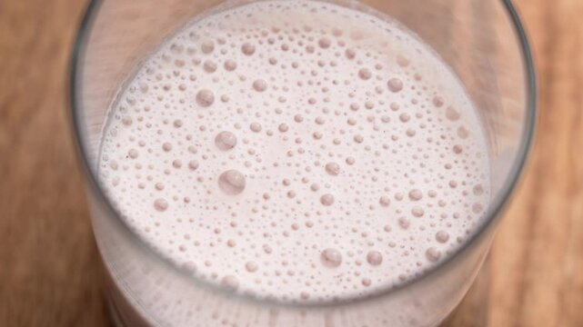 Frothy raspberry protein shake with almond milk in a glass. Bubbles on surface of blended pink drink on textured board. Vegan nutrition. Top view. Rotation