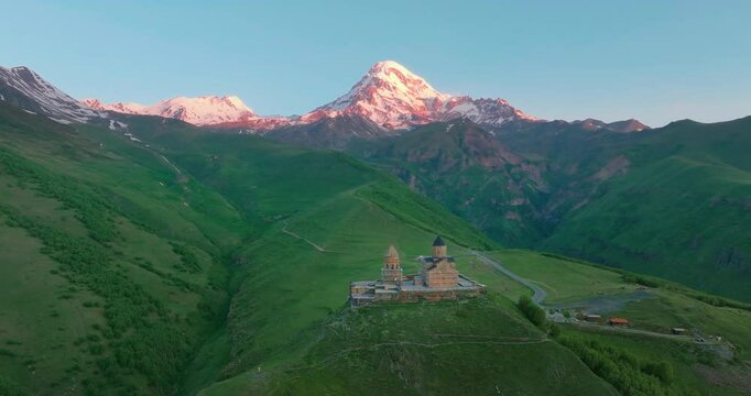 Drone shot of the historic Gergeti Trinity Church located at the foothills of Mount Kazbek with the impressive view of the snow-capped Caucasus Mountains in the background.
