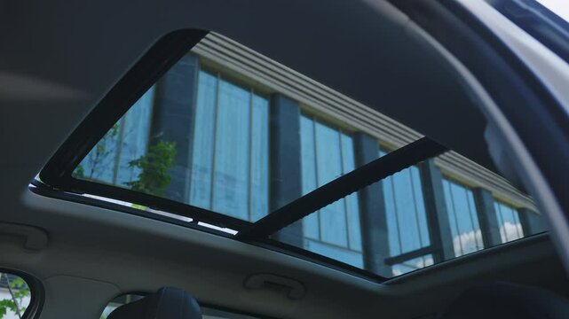 view from below of the opening of a large hatch on a car. The hatch in the roof of a modern SUV opens to get fresh air. The car is parked against the backdrop of beautiful modern glass buildings.