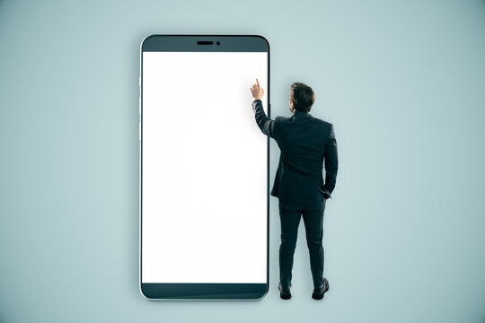Businessman interacting with a giant smartphone with a blank white screen. - Powered by Adobe