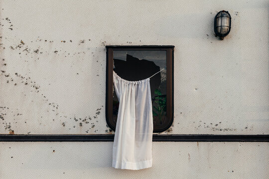una cortina sobresale de una ventana rota de una caravana abandonada. 