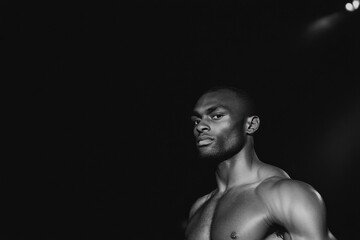 A man with a shaved head stands in front of a black background