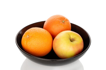 Two juicy oranges and one apple on a black ceramic plate, close-up, isolated on a white background.