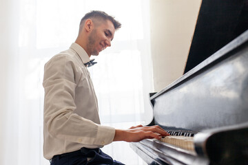 young guy in white shirt plays on old black piano, musician pianist performs melody on acoustic...