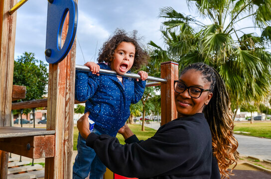 Mother helping daughter playing on monkey bars in playground - Powered by Adobe