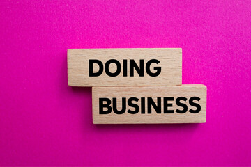 Doing business message written on wooden blocks on pink background. Conceptual doing business symbol. Copy space.