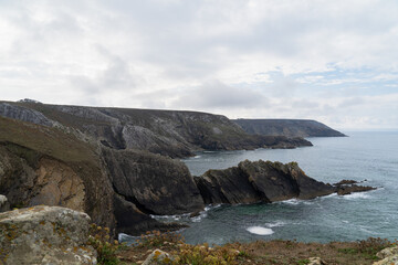 Obraz premium Paysage sauvage sur la presqu’île de Crozon. Sous un ciel bleu parsemé de nuages blancs, les falaises abruptes plongent dans la mer d’Iroise, offrant une vue spectaculaire sur l’océan.