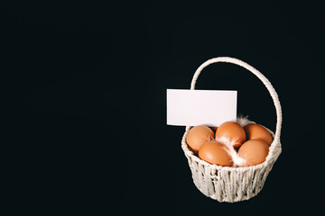 Business card with basket full of hen orange eggs on black background with pussy willow twigs. Copy...