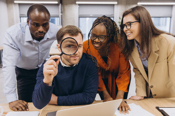 Interracial business team analyzing data on laptop with magnifying glass, working together on...