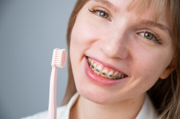 Portrait of a caucasian woman with braces on her teeth holding a toothbrush.