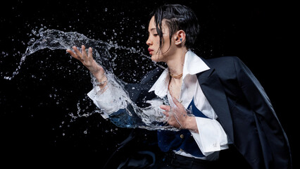 Cinematic portrait of an Asian girl in a black suit with wet hair, elegantly interacting with splashing water on a black background