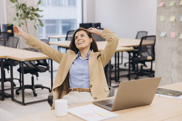 Businesswoman stretching at desk, relaxing after completing laptop work in contemporary workspace