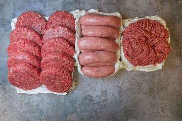 Ready for a grilled selection, including burgers, sausages, and minced beef arranged on a concrete table.
