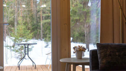 View from house to forest and recreation area with table on winter day. View from the panoramic window. Sofa and table with Scandinavian style decor. Isolated rest