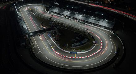 An aerial view of a sleek Formula 1 racetrack at night, with bright neon track lighting guiding the curves.