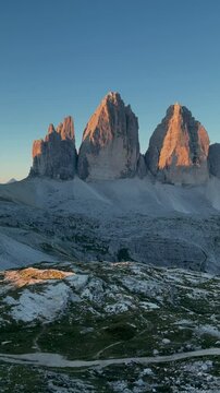 Warm sunlight illuminates the majestic tre cime di lavaredo peaks and refugio locatelli in the italian dolomites