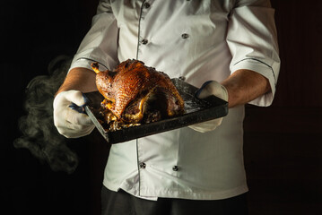 In a dimly lit kitchen, a skilled chef proudly holds a roasted duck on a tray. The rich...