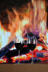 Two glasses of red wine against a burning fire.
