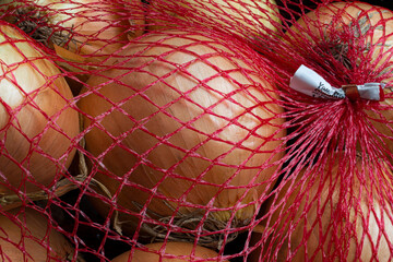A top view image of flavorful large yellow onions packed in a red mesh bag.

