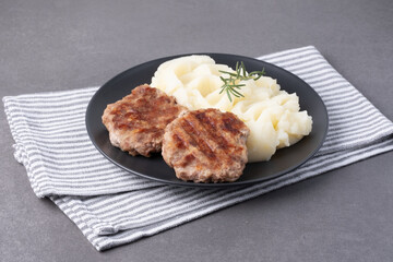 Savory grilled patties with creamy mashed potatoes and fresh rosemary on a dark plate