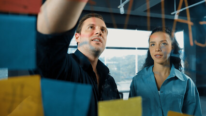 Professional business people discuss about creative marketing idea in modern office. Business team working together to brainstorm financial plan by using sticky notes on glass board. Manipulator.