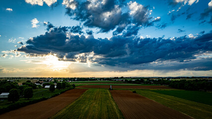 Obraz premium A vibrant sunset casts warm colors over expansive farmland, with lush green fields and patches of clouds creating a picturesque sky. The serene landscape reflects the tranquility of rural life.