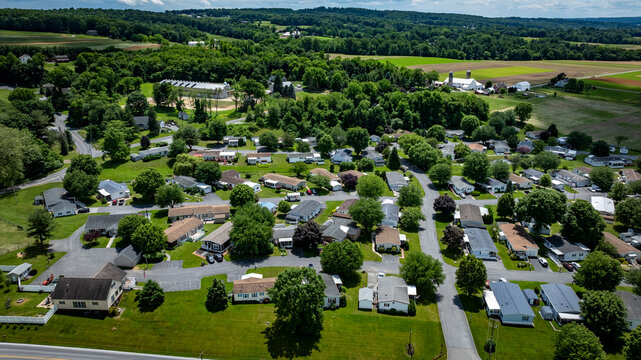 Aerial view of a tranquil rural community featuring various Mobile, Prefab, Manufactured houses situated near lush green fields and trees. The landscape shows harmonious blend of residences farmland.