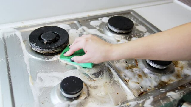 Scrubbing the stove top hard. A hand scrubs a dirty stove top with a cloth, removing grease and grime in a kitchen setting during daylight.
