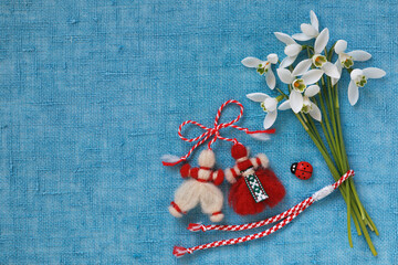 Bouquet of snowdrops and a red and white martenitsa bracelet, figures of a boy and a girl on a blue...