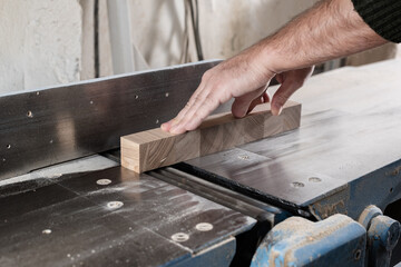 The carpenter handles the ash element with his hands on the electric jointer