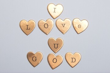 gold heart-shaped objects arranged to spell "I LOVE U GOD" on a gray background. © Elvis