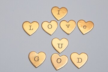 gold heart-shaped objects arranged to spell "I LOVE U GOD" on a gray background.