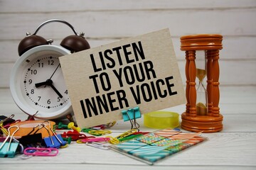 Listen to your inner voice text on paper card with alarm clock and stationary on wooden background