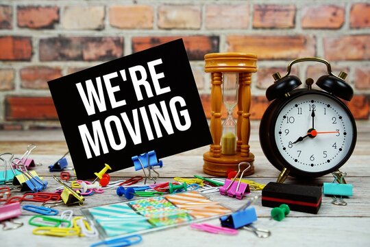 We're Moving text on paper card with alarm clock and stationary on wooden background